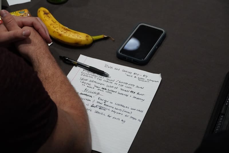 A person writing on paper next to a banana.
