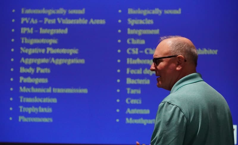 A man standing in front of a blue wall with many words on it.