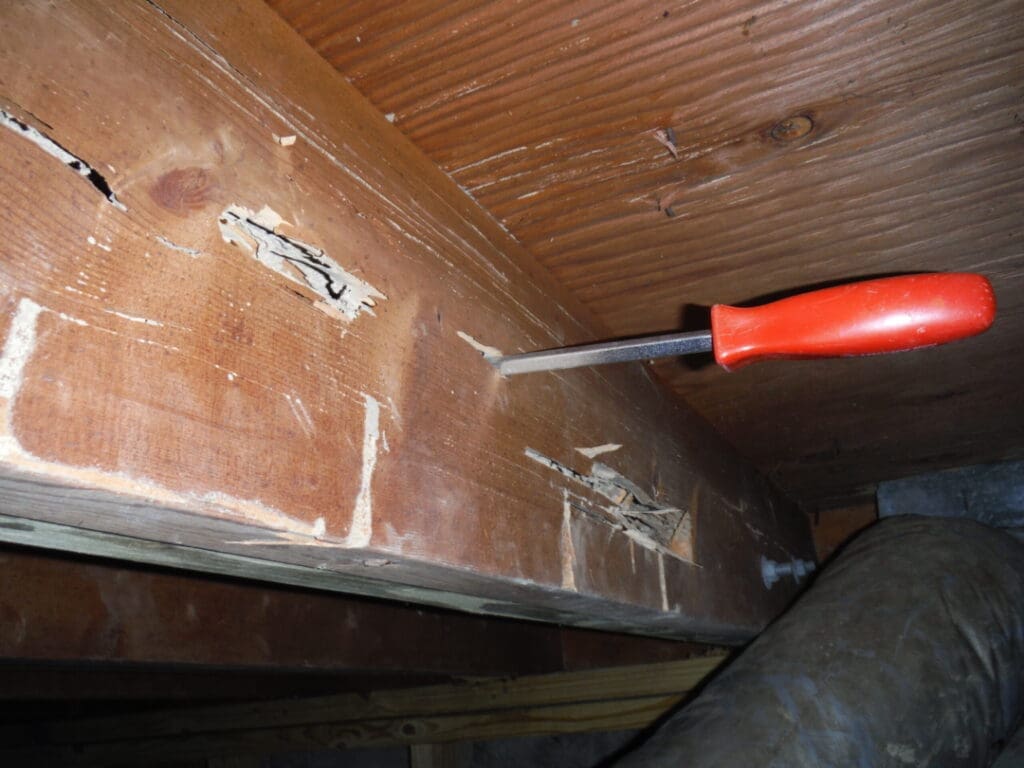 A red handled tool is in the corner of a room.