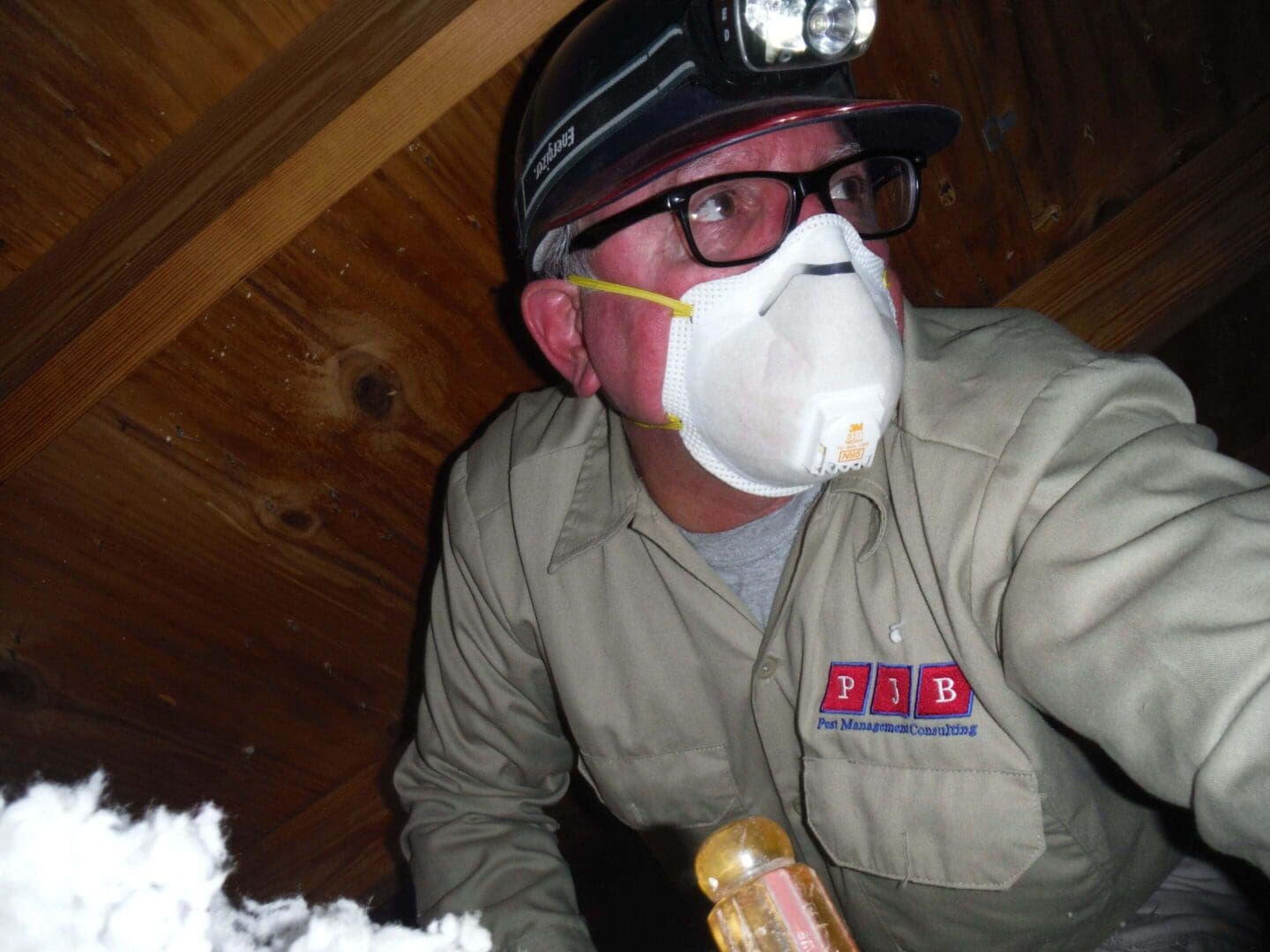 Worker inspecting attic with headlamp and mask.