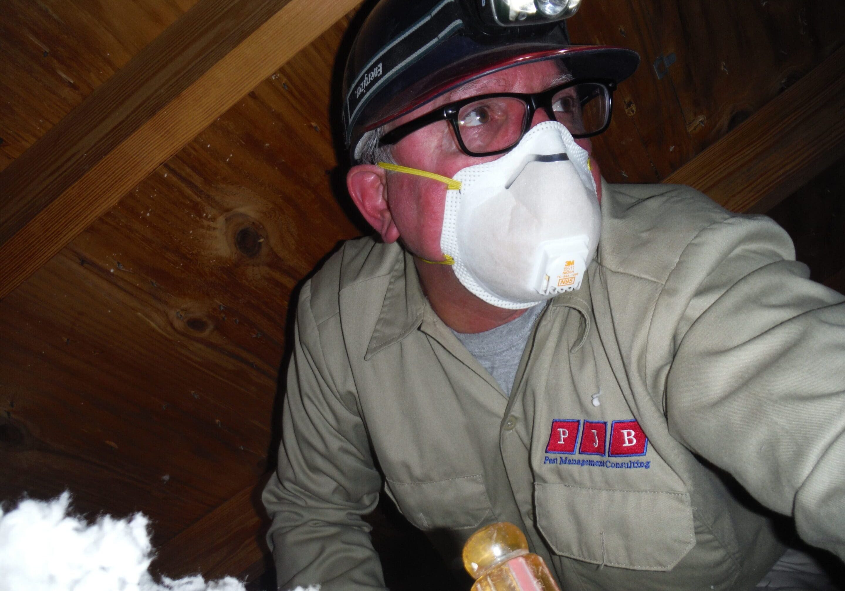 Worker inspecting attic with headlamp and mask.