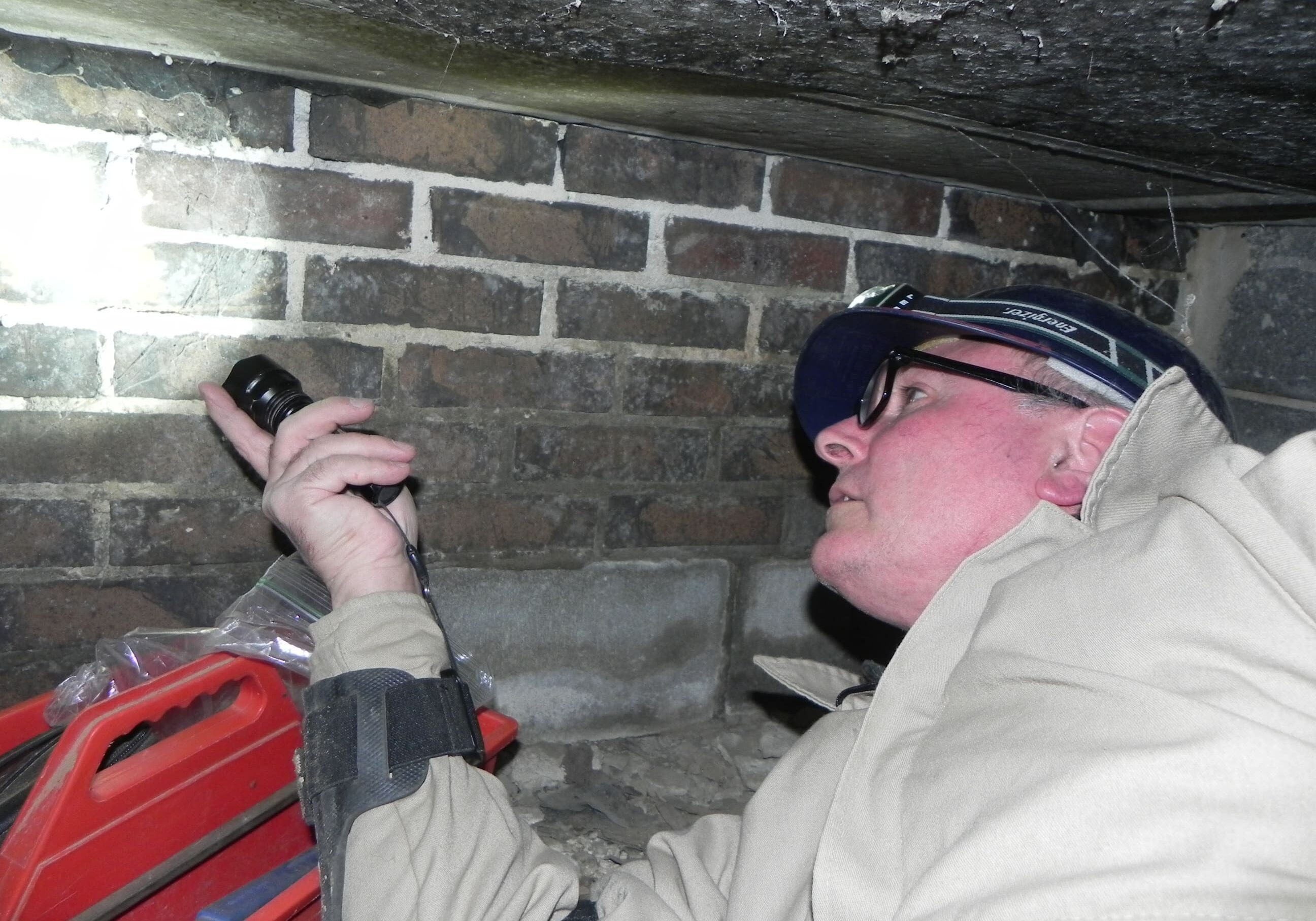 Person inspecting brick wall with flashlight.