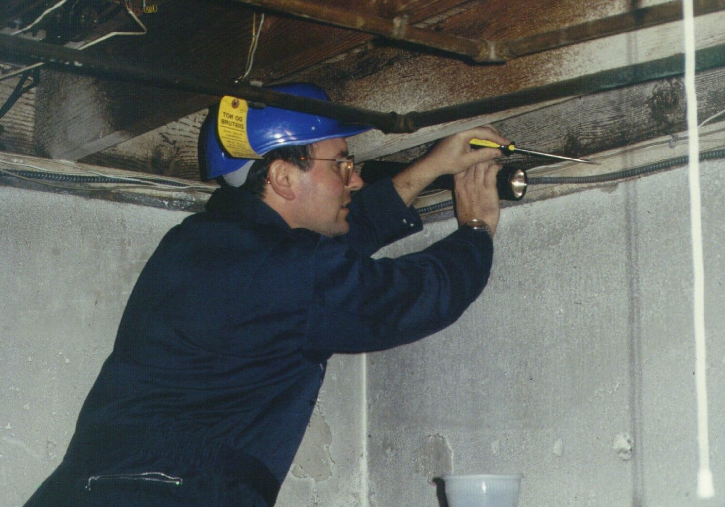 Man inspecting basement ceiling with flashlight.